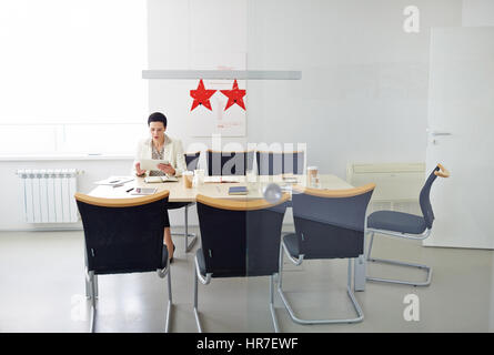 Imprenditrice moderna preparazione per importante incontro seduto da solo al tavolo della sala conferenze e piani di lettura Foto Stock
