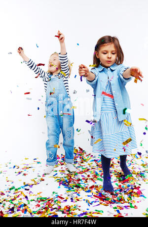 Ritratto in studio di due bambine sia vestito in jeans blu vestiti divertirsi con i confetti, gettando intorno contro uno sfondo bianco Foto Stock