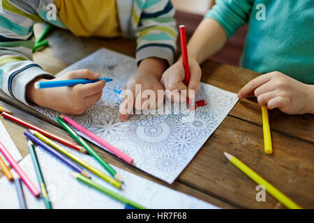 Close-up shot di due coppie di mani piccole mandala colorare con pennarelli, matite di diversi colori e le illustrazioni di cui sul tavolo di legno Foto Stock