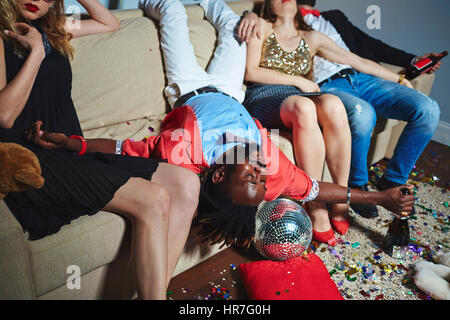 Ritratto di mezza età afroamericane uomo disteso in posizione capovolta sul lettino mentre i suoi amici seduto accanto a lui con gli occhi chiusi dopo la festa notturna Foto Stock