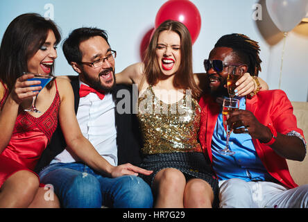 Gioiosa giovane donna in lucido leggermente superiore che abbraccia il suo asiatiche e afro-americani amici mentre in posa per la fotografia durante la bella house party Foto Stock