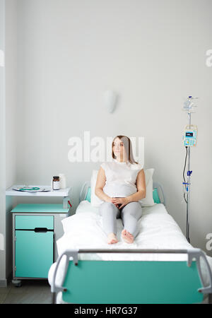 Donna incinta in appoggio sul letto in confortevoli ward e pensando di imminente recapito Foto Stock