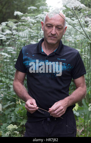 Ritratto di un uomo calvo in posa di fronte a dei fiori con stelo in mano Foto Stock