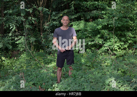 Ritratto di un uomo in piedi tra la sovracrescita di una foresta Foto Stock