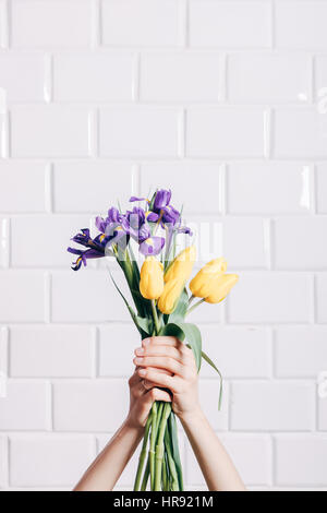 Mani femminili tenendo un mazzo di fiori di giallo e viola Fiori su fondo bianco, inquadratura verticale Foto Stock