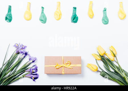 Iridi viola, Tulipani gialli, confezione regalo con fiocco e palloncini su sfondo bianco, vista dall'alto Foto Stock