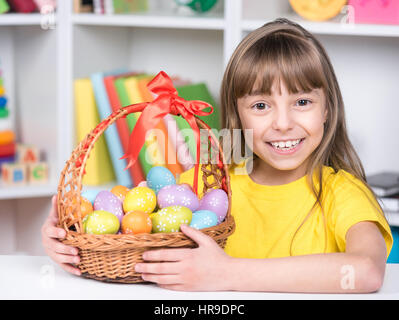 Vacanze di Pasqua - molto carino piccolo ragazza con cesto di uova decorate a casa. Bambino divertirsi e celebrare la festa. Foto Stock
