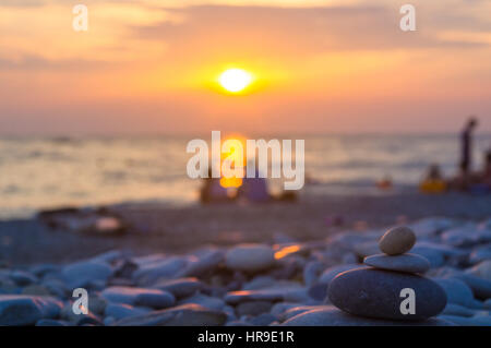 Un giovane e ripiegati a piramide Zen pietre ghiaia sul mare spiaggia al tramonto Foto Stock