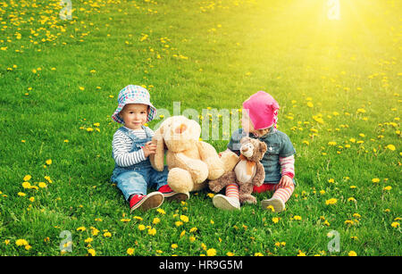 Piccolo Ragazzo e ragazza di cappelli di seduta sul campo con i peluche in estate Foto Stock