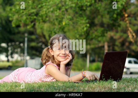 Felice bambina con laptop sdraiati sull'erba Foto Stock