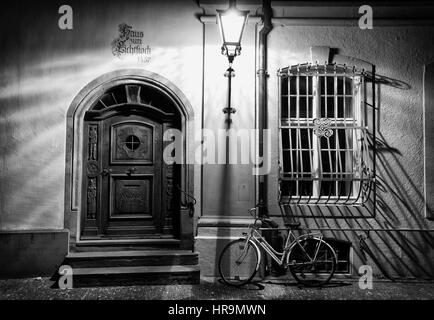 Notte fotografia di una vecchia porta di legno e una bicicletta nel centro storico di Friburgo, Germania Foto Stock