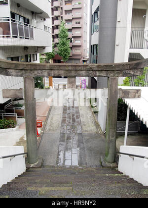 Un torii gate tra edifici appartamento segna l'entrata ad un sacrario scintoista nel centro cittadino di Tokyo in Giappone. Foto Stock