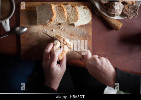 Donna taglia il pane su un vecchio tavolo di legno. messa a fuoco selettiva. Luce naturale dalla finestra Foto Stock