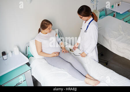 Medico donna misurazione della pressione della donna incinta che giace nel letto di ospedale Foto Stock