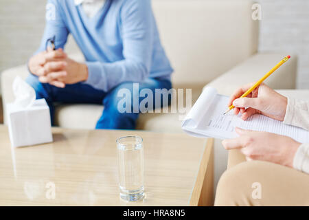 Close-up shot di mani femminili di psicologo rendendo note necessarie nella scheda sanitaria con matita durante la sessione di terapia Foto Stock