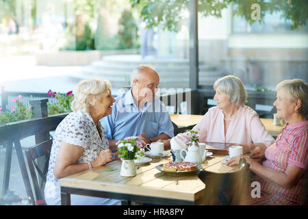 Quattro amici di infanzia riuniti in outdoor cafe dopo una lunga separazione e ricordando storie divertenti dal loro passato Foto Stock