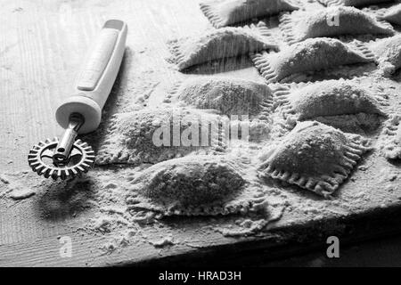 Chiusura del preparato di fresco ravioli su una tavola di legno worksurface con pasta corrugata taglierina Foto Stock