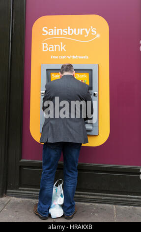 Un uomo con un Sainsburys Bank ATM, London, Regno Unito Foto Stock