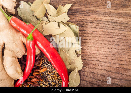 Concetto di stagionatura - assortimento di prodotti freschi e di spezie a secco su sfondo di legno, il peperoncino, foglie di alloro, lo zenzero, il coriandolo Semi Foto Stock