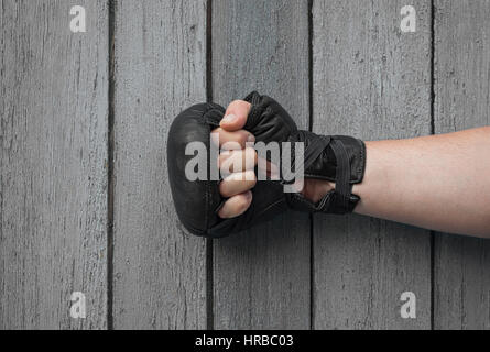 Man a mano in pelle nera guanti di thai boxing rinserrata sul grigio di una squallida sfondo di legno Foto Stock