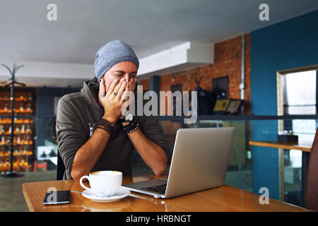 Preoccupato shoked uomo alla ricerca di un portatile presso il cafe Foto Stock