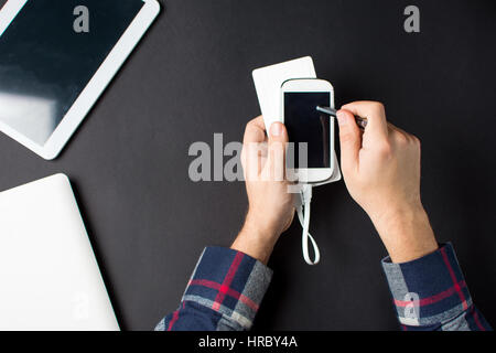 Uomo che utilizza un bianco cellulare collegato ad una banca di potenza Foto Stock