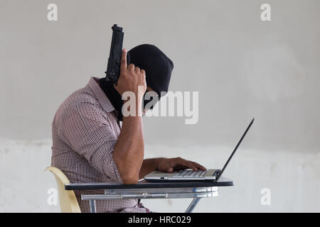 Rapinatore con una pistola e un computer. Foto Stock