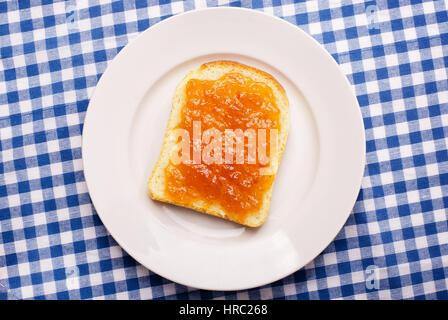 Fette di pane con arancia marmellata di albicocche per la colazione su una piastra, vista da sopra Foto Stock