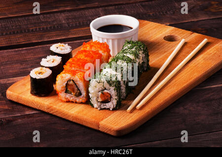 Rotoli di Sushi e salsa di soia con bacchette servita su ardesia di legno in un ristorante Foto Stock