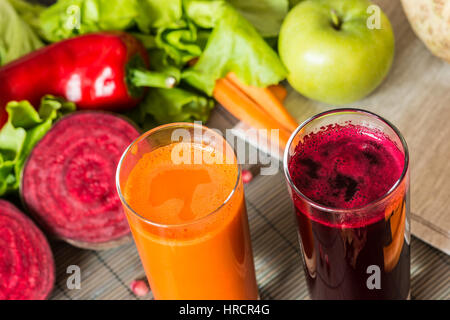 Due bicchieri di diversa del succo di frutta fresco. Barbabietole e carote succhi di frutta su grigio Sfondo legno. Foto Stock