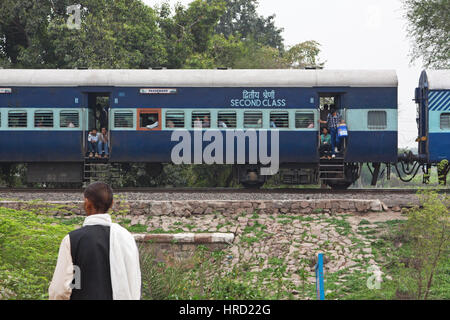 Una lunga distanza di treno passeggeri rallenta avvicinando una strada rurale attraversando nello stato di Madhya Pradesh guardato da un misterioso residente locale Foto Stock