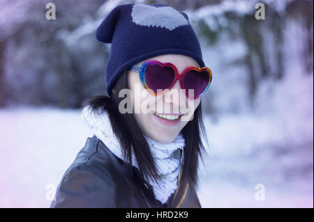 Bella giovane donna sorride nel suo cuore gli occhiali da sole di forma esterna ritratto di moda. / Equipaggiamento per il giorno di San Valentino / bella giovane donna sorride in Foto Stock