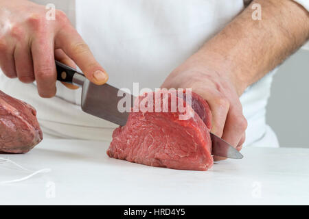 Primo piano delle mani di un macellaio il taglio delle fette di carne cruda off una grande lombo per tournedos Foto Stock