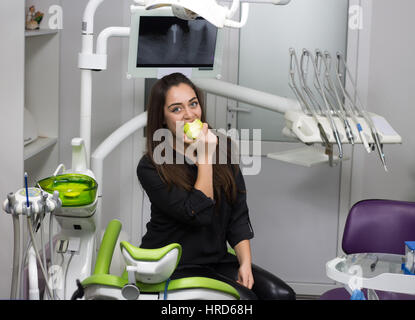 Concetto di dentista. Felice paziente in poltrona odontoiatrica mangiare mela verde Foto Stock