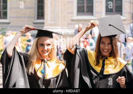 Riga, Lettonia - 1 Luglio 2016: due giovani donne laureati dell'Università di Lettonia vestito in abito di laureati e piazza cappucci accademico che posano per una foto Foto Stock