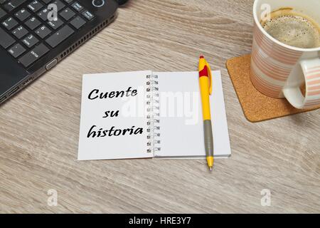 Aprire il notebook con testo spagnolo 'CUENTE SU HISTORIA' (raccontare la tua storia) e una tazza di caffè su sfondo di legno. Vista dall'alto in basso Foto Stock