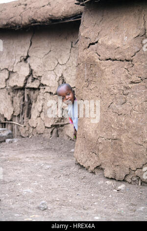 Masai bambino/toddler giocando un peek boo vicino alla sua casa di fango. Kenya. Full frame. 'Maasai un peek boo". Foto Stock