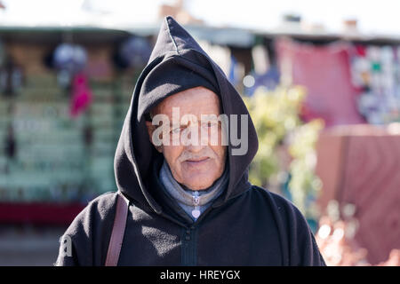 Povero vecchio marocchino uomo ritratto. Indossando il tradizionale mantello con cappuccio. Fornitore stradale vendita di beni economici. Visto il 16 febbraio 2017 al di fuori di Marrakech Foto Stock