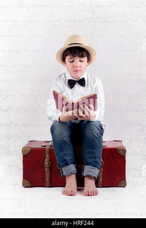 Ragazzo la lettura di un libro seduti in una valigia. Immagine composita di boy leggere un libro Foto Stock