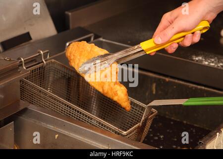 Sollevamento di un pezzo di travagliato cod al di fuori della friggitrice. Foto Stock