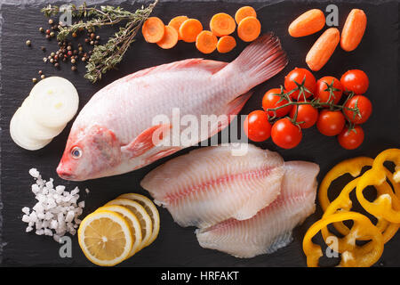 Crudo fresco di tilapia e di ingredienti vegetali, spezie vicino sul tavolo. Vista orizzontale dal di sopra Foto Stock