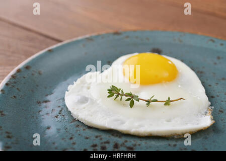 Uovo fritto a forma di cuore sulla piastra blu closeup Foto Stock