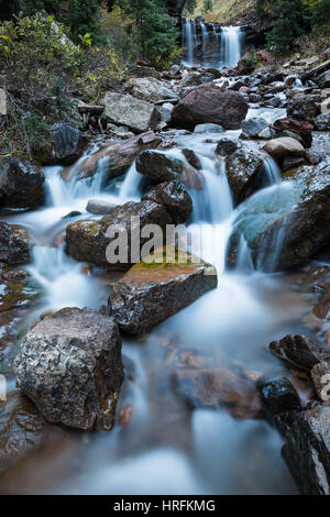 Un piccolo fiume o ruscello attraversa una zona rocciosa in Colorado. Sullo sfondo di una cascata si riversa su una scogliera e un piccolo cascaderuns attraverso il ro Foto Stock