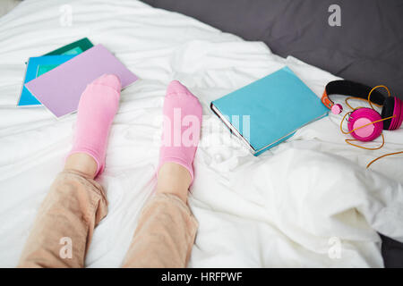 Vista ravvicinata di ragazze in piedi in calze rosa giacente sul letto vicino a libri e le cuffie Foto Stock