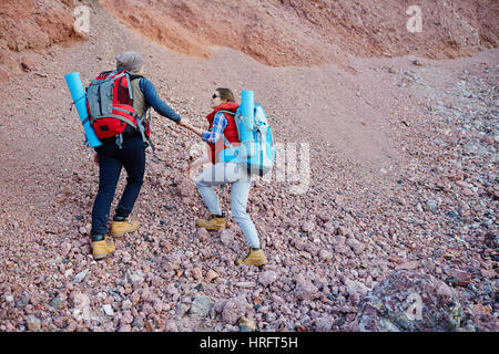 Ritratto di giovane coppia, l uomo e la donna che indossa ingranaggio turistico e grandi zaini andando su per la collina per mano di arrampicata in montagna escursione Foto Stock