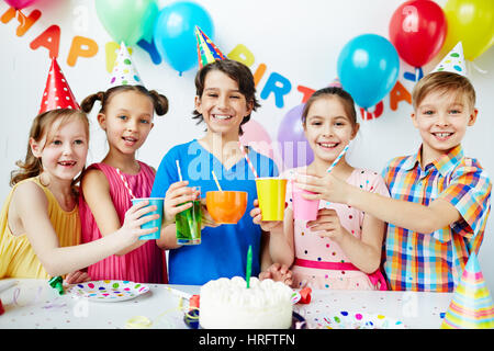 Ritratto colorato di cinque bambini felici insieme permanente in posa, tenendo le loro bevande in celebrazione del compleanno, guardando la fotocamera e sorridente Foto Stock