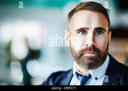 Ritratto di coppia barbuto imprenditore indossando elegante abito formale che guarda lontano su sfocato sfondo blu in office Foto Stock