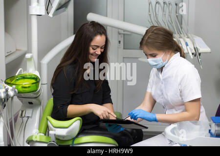 Donne medico dentista è che mostra x-ray denti sul tablet a felice paziente giovane. Dentista o stomatologist indossa abbigliamento medico Foto Stock