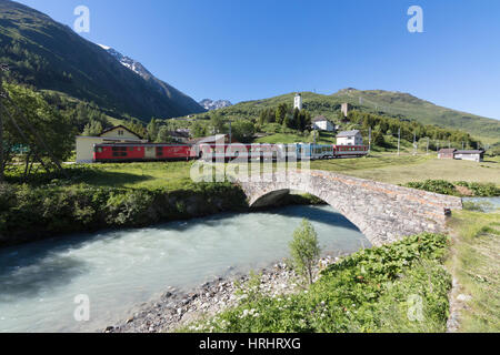 Rosso tipico treno svizzero su Hospental Viadukt circondato da creek e prati verdi, Andermatt, Cantone di Uri, Svizzera Foto Stock