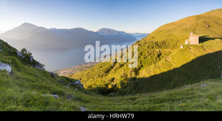 Sun sulla chiesa di San Bernardo si illumina il paesaggio attorno alle acque blu del lago di Como a Alba, Musso, Lombardia, Italia Foto Stock